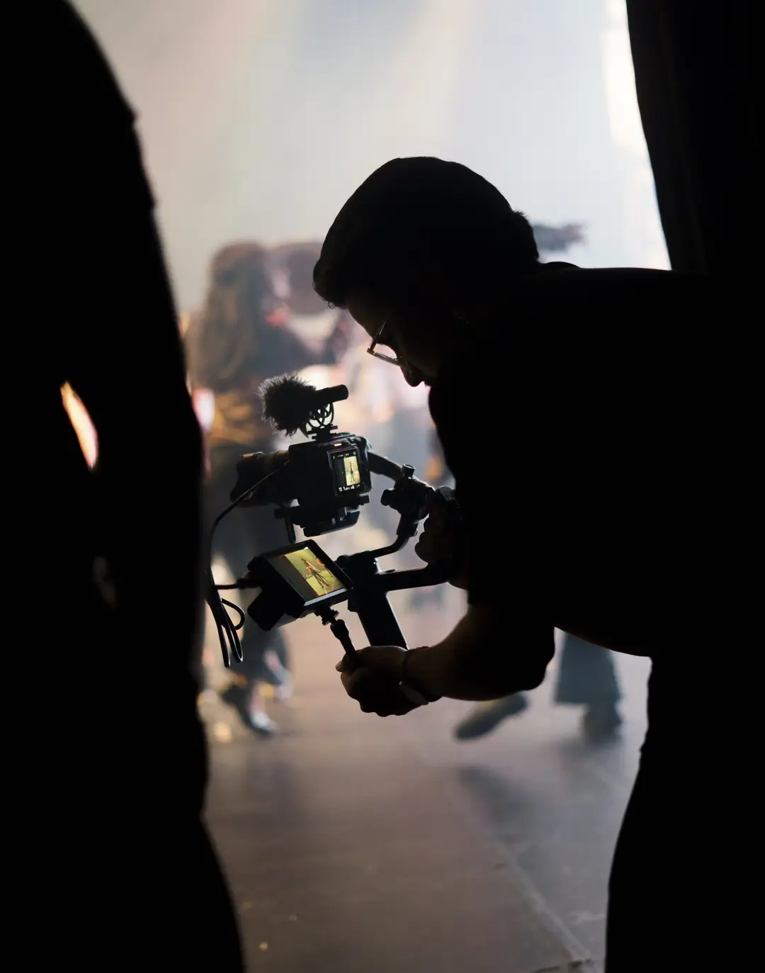 Cinegrafista em silhueta na coxia, contra a luz do palco