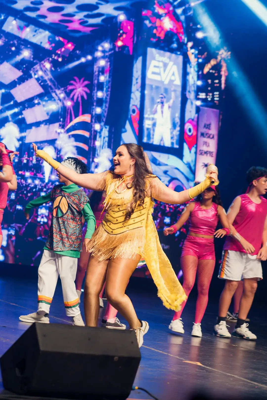 Vocalista de figurino amarelo cantando à frente do telão de axé