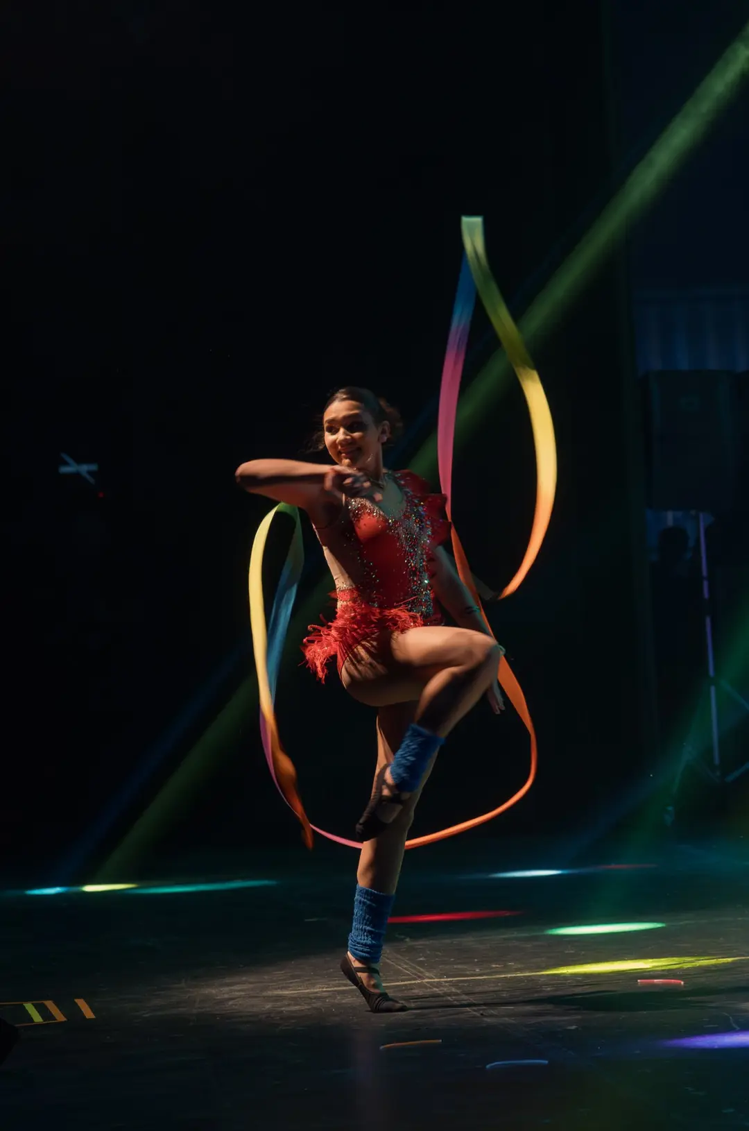 Ginasta girando uma fita colorida no palco escuro